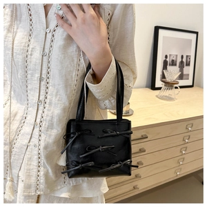 Detail of a black leather handbag featuring 3D bow accents held by a woman in a beige shirt