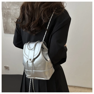 Rear view of model wearing a glossy silver metallic backpack with chain straps and turn-lock