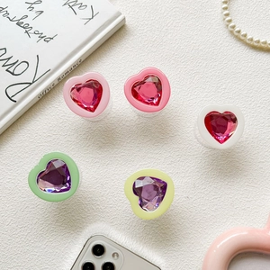 Flat lay of colorful heart-shaped gem phone grips on white textured background
