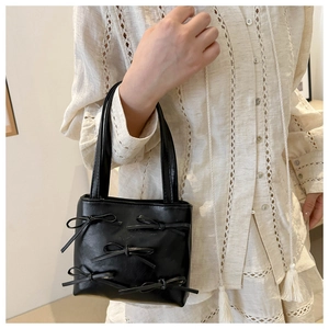 Detail of a black glossy PU leather handbag with five bows worn with a lace blouse