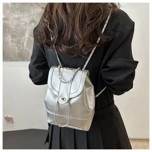 Detail of metallic silver backpack featuring chain straps and round metal twist lock