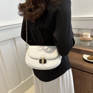 Minimalist white saddle bag with gold chain strap shown on model in stylish interior