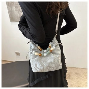 Detail of crossbody bucket bag with marble texture and multicolor beaded handle on model