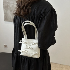 Minimalist white bow small square bag with stylish armpit strap shown on a black dress