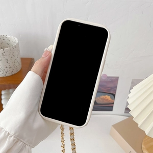 Creamy white phone case with gold braided chain strap shown in a warm home setting