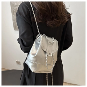 Modern silver metallic backpack featuring chain straps and flap closure on model