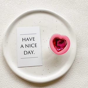 Detailed view of heart-shaped phone grip with red gemstone on a ceramic plate