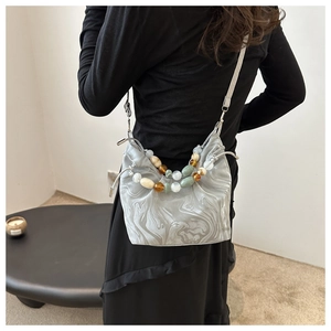 Detail of grey marble bucket bag featuring colorful beaded handle and slim shoulder strap