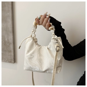 Detail of crossbody bucket bag featuring beaded handle and marble texture pattern