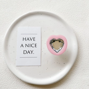 Macro view of a pink heart-shaped phone grip with a faceted crystal center on a ceramic plate