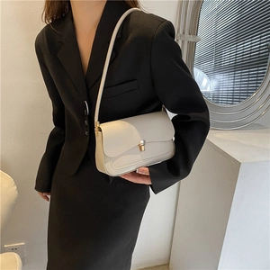 Minimalist cream leather shoulder bag with gold metal clasp on a model in a modern interior