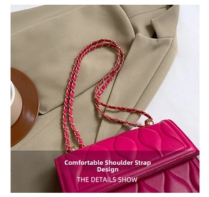 Detail of rose red quilted square bag with gold chain strap on a chic blazer background