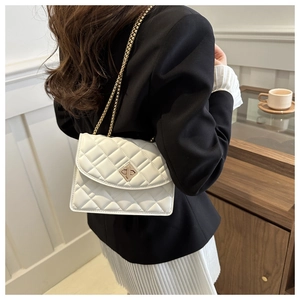 Close-up of white quilted chain bag with gold diamond lock worn by a model in soft light