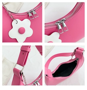 Detail view of hot pink half-moon bag featuring silver zippers and white flower pendant