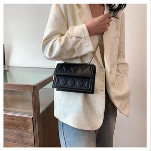 Detail of black quilted crossbody bag with gold chain strap worn by a female model