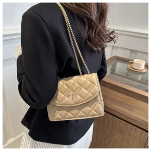 Detail of beige quilted shoulder bag with gold chain strap and metal twist lock on model