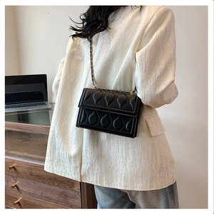 Close-up of black quilted crossbody bag with heart pattern and gold chain strap detail