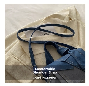 Detail of denim crossbody bag featuring a stitched shoulder strap and metal lobster clasp