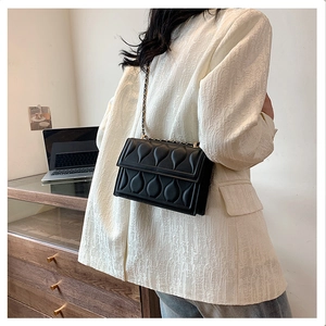 Detail of black quilted crossbody bag with golden chain strap on a model in an office