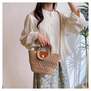 Close-up of woven straw tote bag with brown leather flap and pearl buckle detail