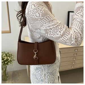 Detail of brown leather shoulder bag with gold metal buckle on a female model