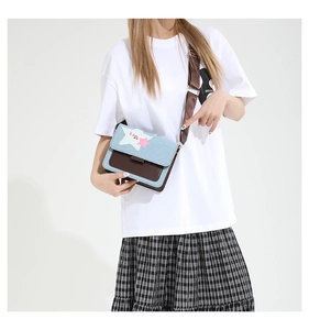 Detail of denim and brown leather crossbody bag with star patch and adjustable strap