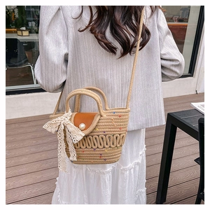 Detail of straw woven bucket bag featuring pearl closure and elegant white lace bow