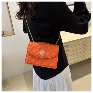 Detail of bright orange quilted crossbody bag with gold twist lock on a model