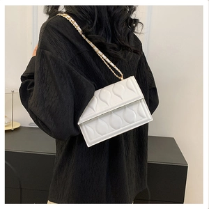 Detailed view of white crossbody bag featuring waterdrop embossed texture and gold chain strap