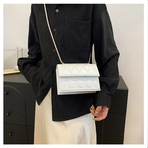 Detail of white quilted crossbody bag with heart pattern and elegant gold chain strap