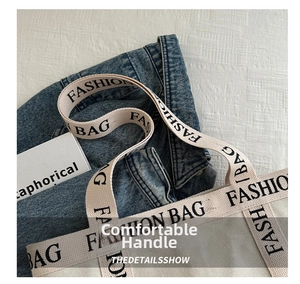 Detail of canvas tote bag featuring woven handle with black FASHION BAG letter print