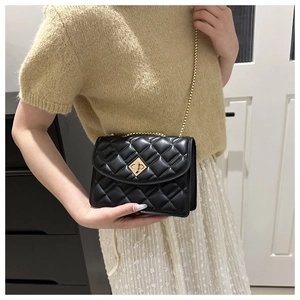 Detail of a black quilted chain bag with gold lock worn on the shoulder in a lifestyle setting
