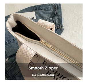 Detail of a smooth metal zipper on a beige canvas tote bag with FASHION BAG lettering