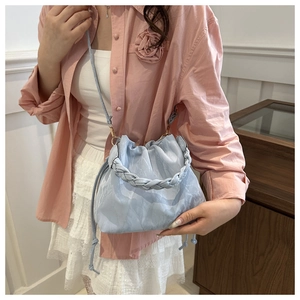 Close-up of light blue pleated bucket bag featuring a thick woven handle and slim shoulder strap
