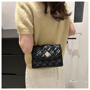 Close-up of black quilted shoulder bag featuring a gold floral clasp and fine chain strap