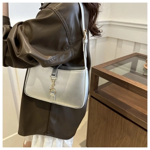 Detail of silver metallic shoulder bag with golden hook buckle worn over a brown leather jacket