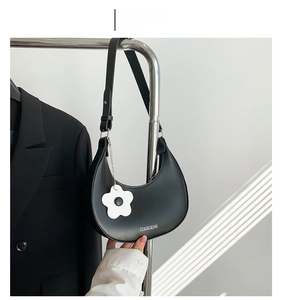 Detail view of black crescent shoulder bag with white flower charm and brand logo