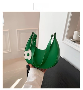 Detail view of green hobo bag featuring a white flower charm and elegant metal chain strap