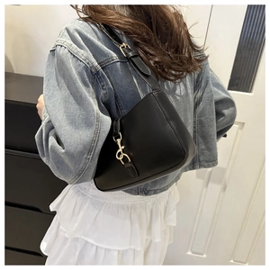 Detail of a black leather underarm bag with gold hook accents worn by a model