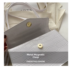Close-up of the bright gold magnetic metal buckle on a white crocodile pattern handbag