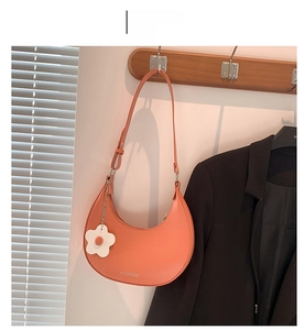 Detail of orange crescent shoulder bag with matte leather finish and flower pendant