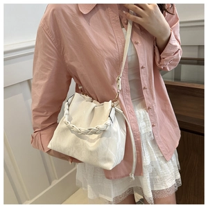 Detail of white pleated bucket bag with braided handle and adjustable shoulder strap