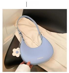 Close-up of light blue crescent underarm bag with gold logo and flower charm detail