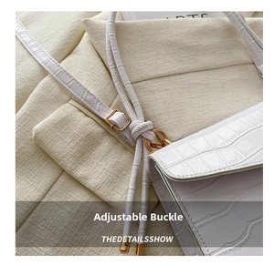 Detail of adjustable gold buckle and croc-embossed texture on a white crossbody bag