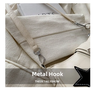 Detail of silver hardware hooks and black star patch on beige leather handbag