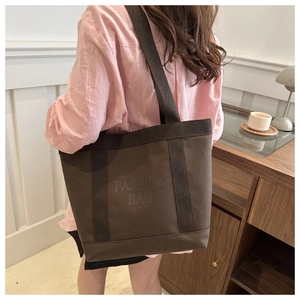 Detail view of large dark brown canvas tote bag with fashion bag text on shoulder