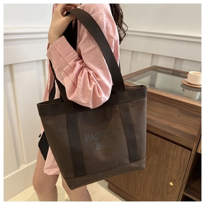 Detail of a dark brown canvas tote bag with 'FASHION BAG' print and wide handles