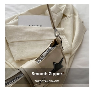 Detail of silver smooth zipper and star patch on cream leather crossbody bag