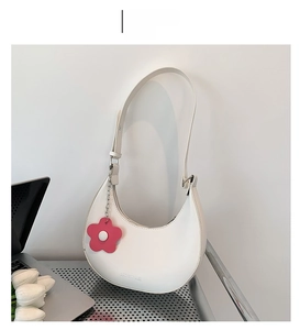White crescent underarm bag with adjustable strap and pink flower charm on white desk