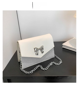 Dettaglio della borsa a busta in pelle bianca e glitter argento con fiocco e catena